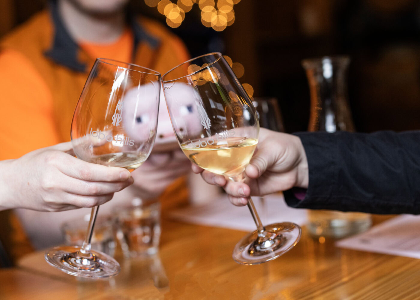 Two people clinking wine glasses with white wine at Lobo Hills Wine Co. celebration.