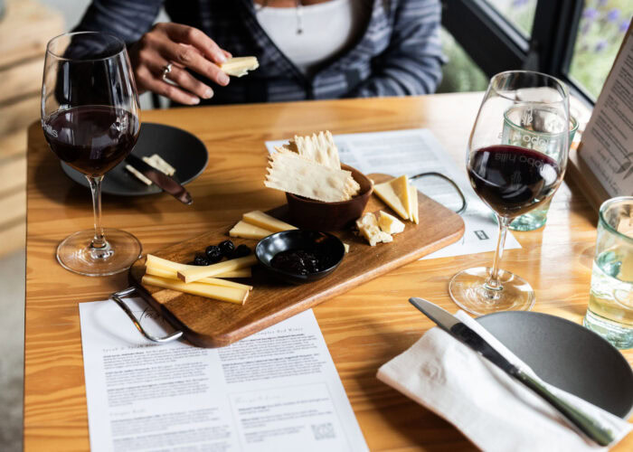 Tasting cheese and wine at Lobo Hills Wine Co. with cheese platter, red wine glasses, and tasting menu on a wooden table.