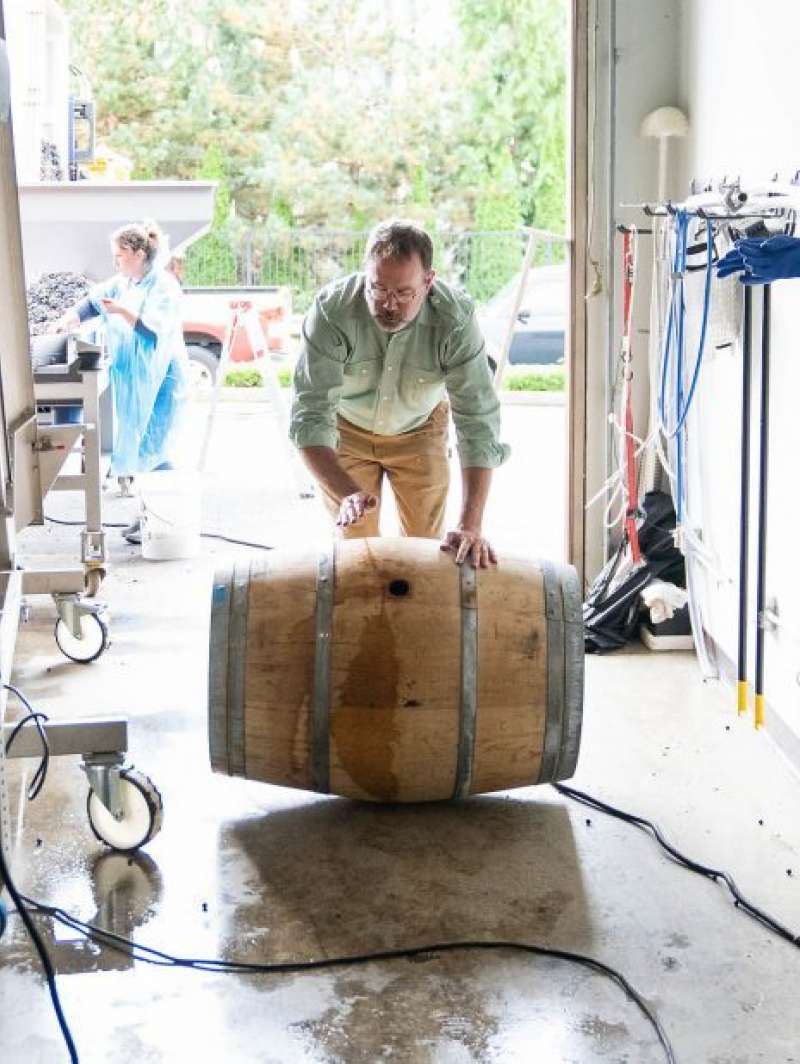 Man rolling a wine barrel inside Lobo Hills Wine Co. winery, showcasing wine production process.