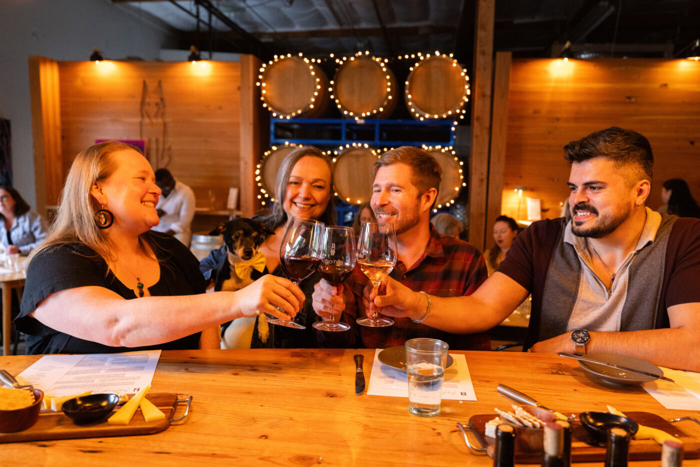 Group of friends enjoying wine at Lobo Hills Wine Co., smiling and toasting in a cozy, rustic winery setting.