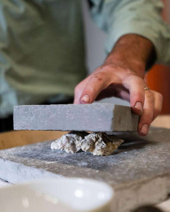 Depict image accurately for accessibility. A person in a green shirt is working with stone or tile, using a trowel or similar.