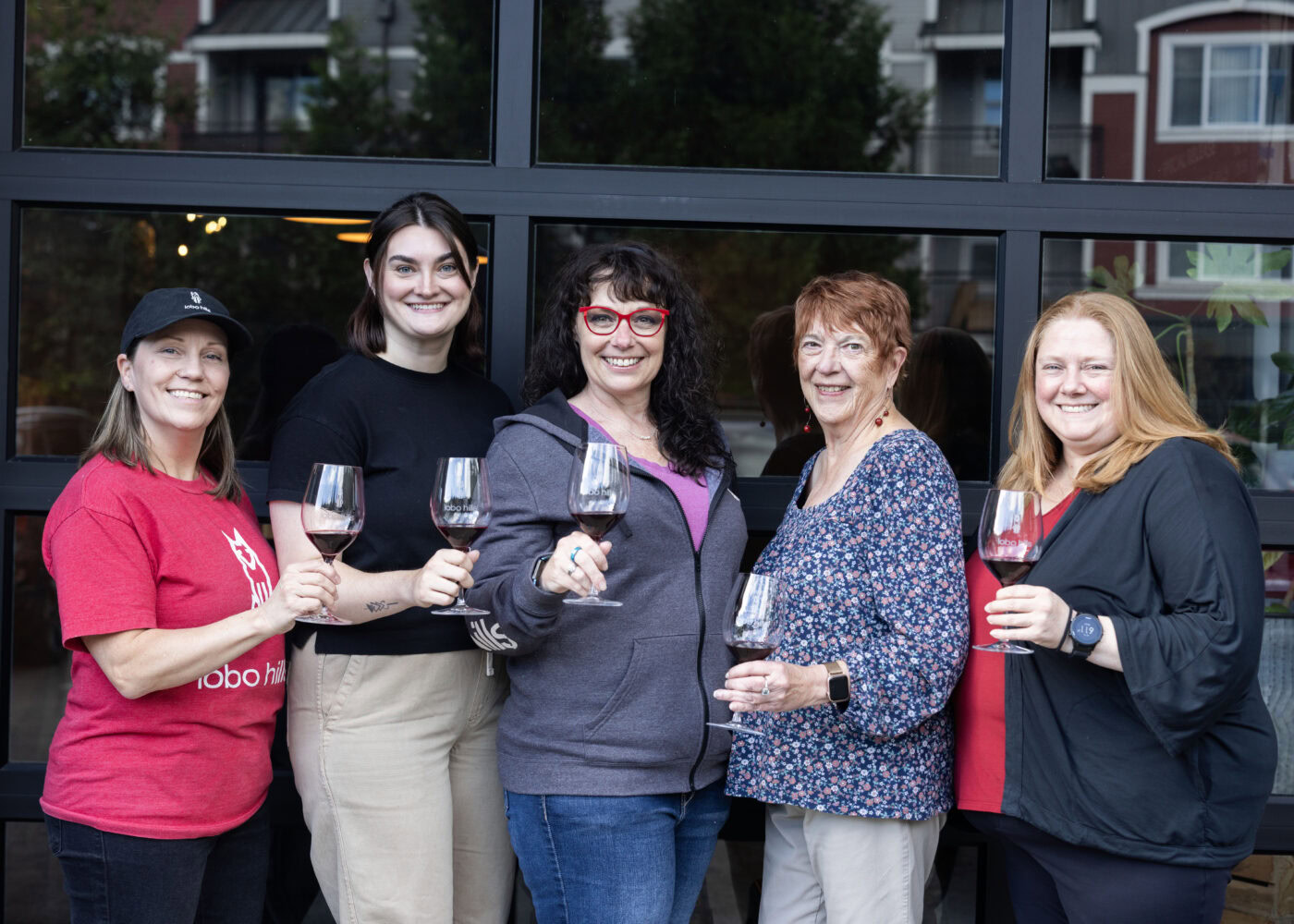 Group of women enjoying wine at Lobo Hills Wine Co. event, smiling and holding glasses, in front of a modern building.